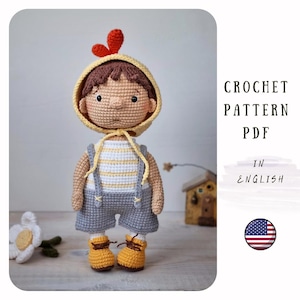 May include: Crochet pattern PDF in English for a cute crocheted doll wearing a yellow and brown hat with a red comb, a striped shirt, blue overalls, and yellow shoes. The doll is standing on a table with a flower and a small wooden house in the background.