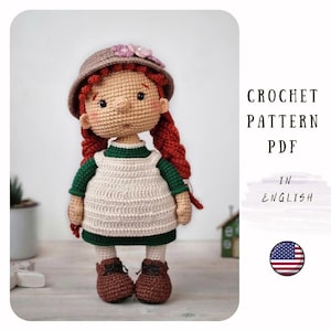 May include: A crocheted doll with red braided hair, wearing a green and cream-coloured dress, brown shoes, and a hat with flowers. The image includes the text "CROCHET PATTERN PDF IN ENGLISH" and an American flag.