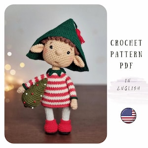 Könnte beinhalten: Häkelanleitung PDF in Englisch für eine süße Elfen-Amigurumi-Puppe, die einen kleinen Weihnachtsbaum hält. Der Elf trägt einen grünen Hut, einen rot-weiß gestreiften Pullover und rote Schuhe.