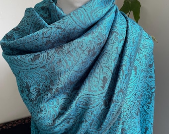 May include: A teal and black paisley patterned shawl draped over a white mannequin head. The shawl is made of a soft fabric and has a detailed design. The color is a vibrant teal with black accents, creating a striking contrast.