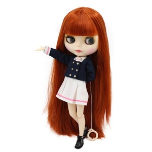 May include: A fashion doll with long, red hair and large eyes. The doll wears a navy blue jacket with gold buttons, a white pleated skirt with pink trim, and black boots. A string with a wooden ring is attached.