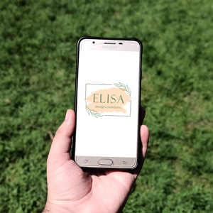Może przedstawiać: Smartfon wyświetlający logo firmy projektowej o nazwie "ELISA design creations". Logo zawiera tło w stylu akwareli z zielonymi liśćmi i biały prostokąt z nazwą firmy.