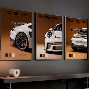 Puede incluir: Tres carteles enmarcados de coches Porsche GT3 RS. Cada cartel presenta un coche deportivo blanco sobre un fondo marrón. Los carteles tienen la palabra "PORSCHE" en la parte superior y una paleta de colores en la parte inferior. Los carteles se muestran en una pared gris oscuro.