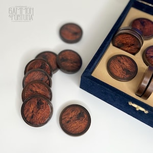 Puede incluir: Piezas de juego de madera con veta de madera de color marrón rojizo. Las piezas redondas tienen un borde marrón oscuro, algunas están en una caja de terciopelo azul. El logotipo "GAMMON & FORTUNA" está en la esquina superior izquierda.