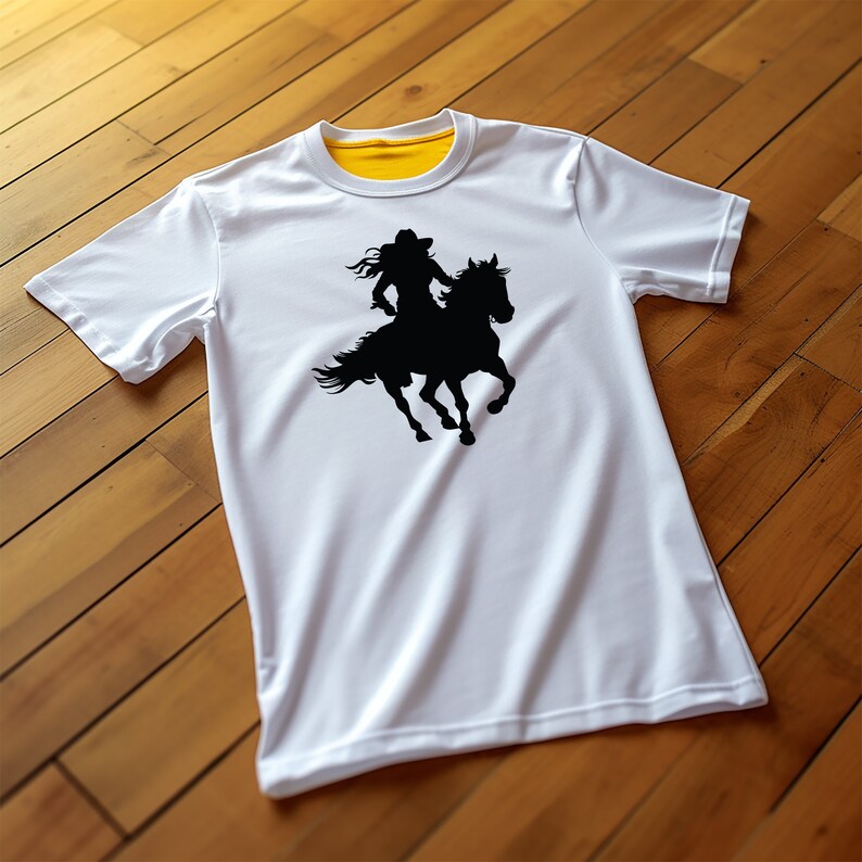 May include: White t-shirt with a black silhouette of a person riding a horse. The rider is wearing a cowboy hat. The shirt has a yellow collar and white sleeves. The shirt is displayed on a wooden surface.