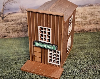 May include: A miniature wooden general store building with a brown facade, a green sign that reads "General Store", and two windows with white frames.