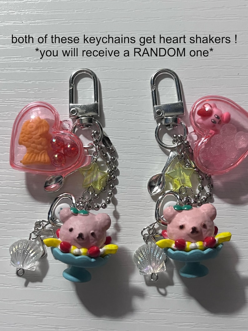 Puede incluir: Dos llaveros de coraz&oacute;n rosa con un dije de helado con forma de oso y un dije de concha. Un dije tiene un pez dorado adentro y el otro tiene un personaje de dibujos animados rosa. El texto en la imagen dice "&iexcl;ambos llaveros tienen agitadores de coraz&oacute;n! *recibir&aacute;s uno ALEATORIO*"