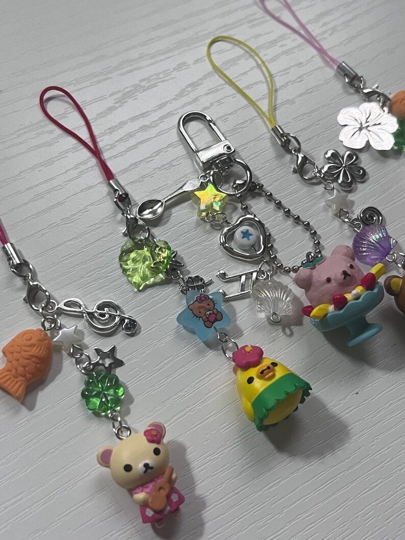 Puede incluir: Una colecci&oacute;n de abalorios para tel&eacute;fono de colores con personajes de dibujos animados, una cuchara, una nota musical, una estrella, un tr&eacute;bol, una concha, un pez y un coraz&oacute;n. Los abalorios est&aacute;n unidos a cuerdas de colores.