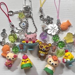 Puede incluir: Una colecci&oacute;n de llaveros con dijes coloridos que representan osos de dibujos animados, un pollito y un pez. Los dijes est&aacute;n unidos a cadenas plateadas y cuerdas de colores.