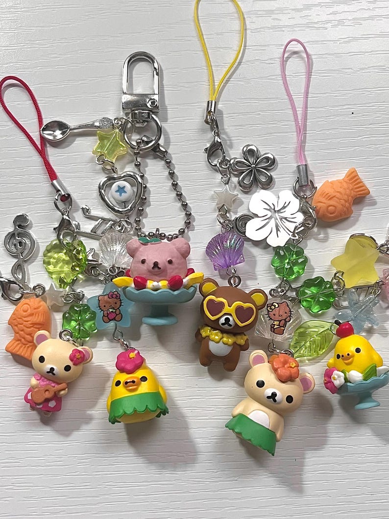 Puede incluir: Una colecci&oacute;n de llaveros con dijes coloridos que representan osos de dibujos animados, un pollito y un pez. Los dijes est&aacute;n unidos a cadenas plateadas y cuerdas de colores.