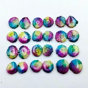 May include: A collection of twenty-four circular, flat, multi-colored solar quartz slices arranged in four rows. Each slice features a vibrant, tie-dye-like pattern of blue, purple, green, and yellow hues with a central core and radiating lines.