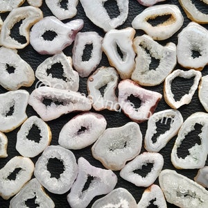 May include: A collection of white agate slices with a natural crystal formation in the centre. The slices are translucent and have a slight pink hue.