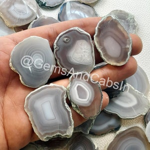 May include: A collection of gray agate slices with white and brown banding. The slices are various shapes and sizes and have a natural, polished finish.