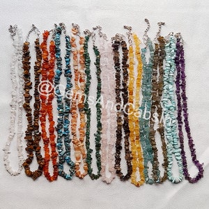 以下が含まれることがあります： 白、オレンジ、茶色、青、緑、ピンク、紫など、さまざまな色の15種類の宝石チップネックレスのセット。ネックレスは、小さく不規則な形の宝石チップで作られています。