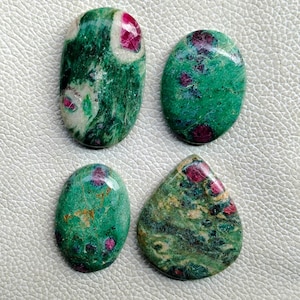 Puede incluir: Cuatro piedras preciosas pulidas con una mezcla de tonos verdes y rojos. Las piedras tienen formas variadas, incluyendo ovaladas y en forma de lágrima. Las inclusiones rojas están dispersas por la base verde, creando un patrón único. Estas piedras probablemente se utilizan para la fabricación de joyas.