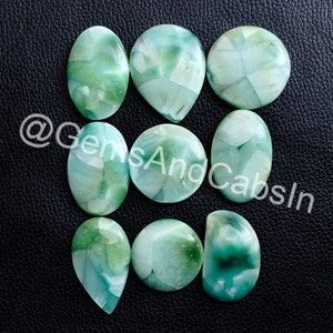 May include: Nine green and white cabochon gemstones with a swirling pattern. The gemstones are arranged in a grid pattern on a black surface.