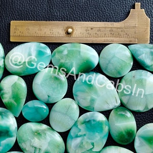 May include: A collection of 14 green and white cabochons, some with a pear shape and others oval, with a ruler for scale.
