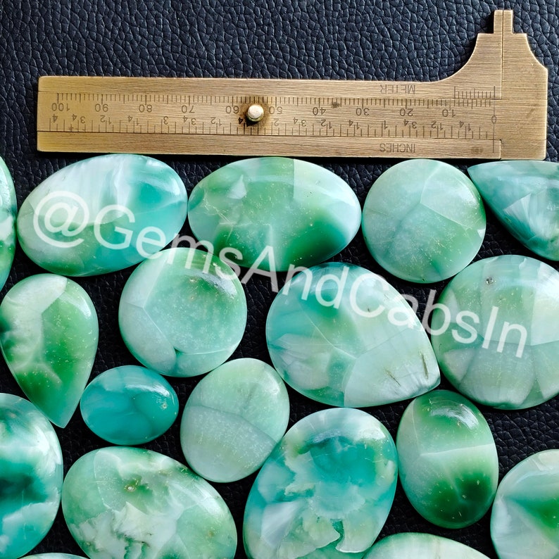 May include: A collection of 14 green and white cabochons, some with a pear shape and others oval, with a ruler for scale.