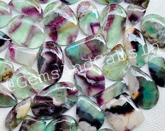May include: A collection of 20+ green, purple, and white fluorite cabochons. The cabochons are various shapes and sizes, with some having a more opaque appearance and others being more translucent. The cabochons are all polished and have a smooth, glossy finish.
