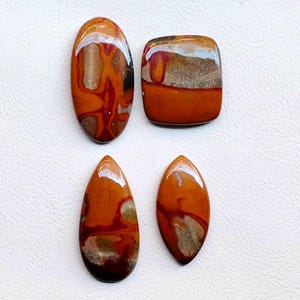 Puede incluir: Cuatro piedras preciosas pulidas en tonos marrón, rojo y beige. Las formas incluyen un óvalo, un cuadrado, una lágrima y una forma de hoja. Las piedras tienen un acabado brillante y una apariencia natural y terrosa.