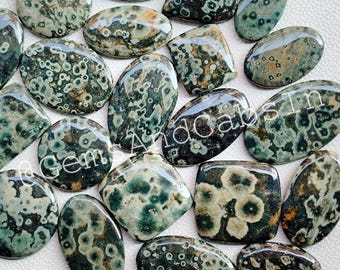 May include: A collection of 15 green and brown ocean jasper cabochons with a variety of shapes and sizes. The cabochons have a unique pattern of white and black spots.