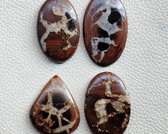 May include: Four polished gemstones in various shapes: two ovals, one teardrop, and one oval. The stones feature a mix of brown, black, and white patterns, with a polished, glossy finish. The gemstones are set against a white background.