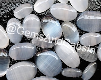May include: A collection of oval-shaped, white, and gray gemstone cabochons with a striated pattern. The stones are smooth and polished, with a slight sheen.