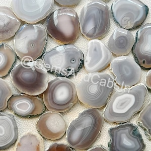 May include: A collection of grey and white agate slices with natural patterns. The slices are smooth and polished, with a variety of shapes and sizes.