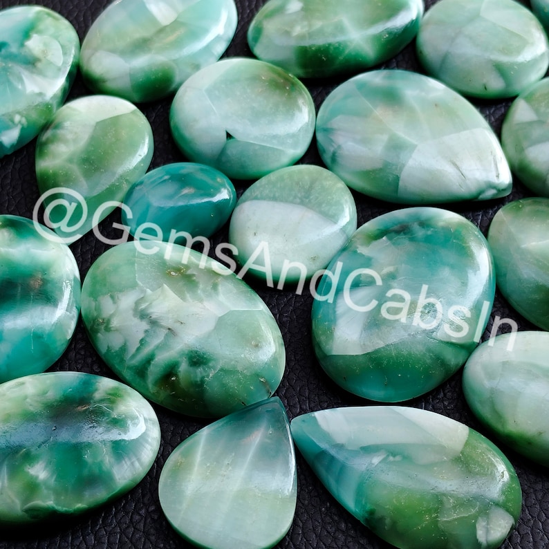 May include: A collection of green and white cabochon gemstones with a variety of shapes and sizes. The stones have a translucent appearance and a swirling pattern.