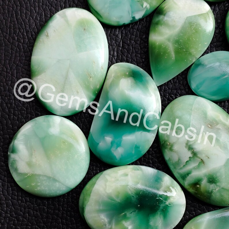 May include: Assortment of green and white cabochon gemstones with a swirling pattern. The stones are oval and round in shape. @GemsAndCabsIn