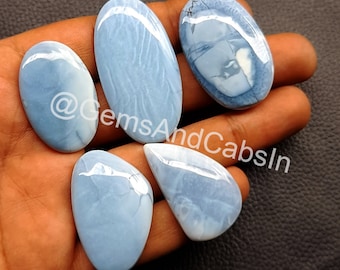 May include: Five blue opal cabochons, each with a unique pattern of white and blue swirls. The cabochons are oval and teardrop shaped, and they are arranged in a cluster on a hand.