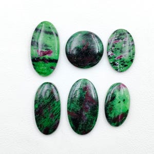 Peut inclure: Six cabochons polis en zoïsite avec des inclusions de rubis, présentant un mélange de motifs vert vif, noir profond et rouge magenta. La collection comprend cinq pierres de forme ovale et une pierre circulaire, toutes aux surfaces lisses et brillantes.