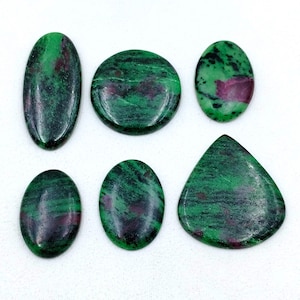 May include: Six polished gemstones in various shapes: oval, round, and teardrop. The stones feature a deep green base color with swirling patterns and patches of dark red. The gemstones are displayed against a white background.