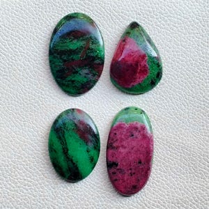 May include: Four polished gemstones with a mix of colors. Two are oval-shaped, one is teardrop-shaped, and one is oval-shaped. The stones feature a combination of green, red, and black hues, with a glossy finish. These gemstones are suitable for jewelry making.