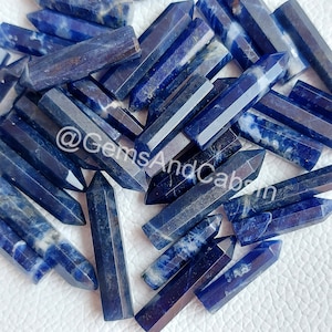 May include: A collection of blue and white Sodalite crystal points. The points are smooth and polished, with a variety of shapes and sizes. The crystals are arranged in a random pattern, with some overlapping. The background is a white surface.