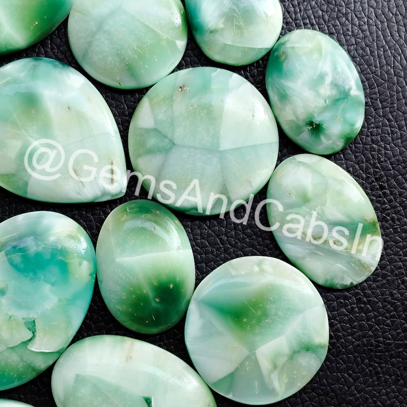May include: A collection of green and white cabochon gemstones. The stones are oval and round in shape and have a variety of patterns and textures.