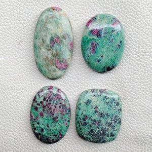 May include: Four polished ruby in zoisite gemstones. The stones have a mix of green and pink hues, with a speckled appearance. The shapes include oval and rectangular forms, showcasing natural variations in colour and texture.