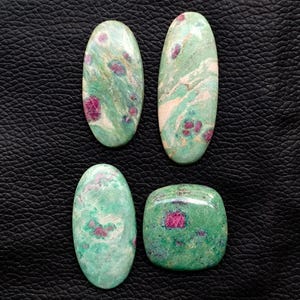 May include: Four polished gemstones with a mix of green and pink hues. Two are oval-shaped, one is rectangular, and one is square. The gemstones have a marbled appearance with a mix of colors.