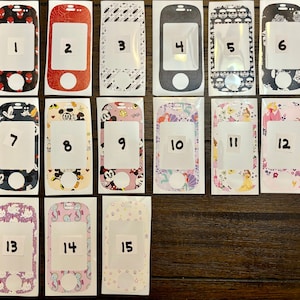 May include: Fifteen different phone skin designs. The designs include a variety of themes, including superheroes, cartoon characters, and abstract patterns. The skins are all in a rectangular shape and are numbered 1 through 15.