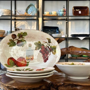 Könnte beinhalten: Ein Set aus vier weißen Keramik-Servier-Schalen mit einem Blumendesign mit Trauben, Feigen und Äpfeln. Die Schalen sind ineinander verschachtelt und haben einen rustikalen, ländlichen Stil.