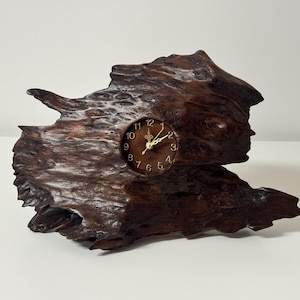 May include: A distinctive wooden clock featuring a brown clock face and gold hands. The clock is set within a piece of dark brown, textured wood. The wood has a natural, organic form, and the clock face displays the numbers 1 to 12.