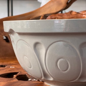 May include: A large, gray ceramic mixing bowl with a textured, rippled design. The bowl is sitting on a wooden surface.