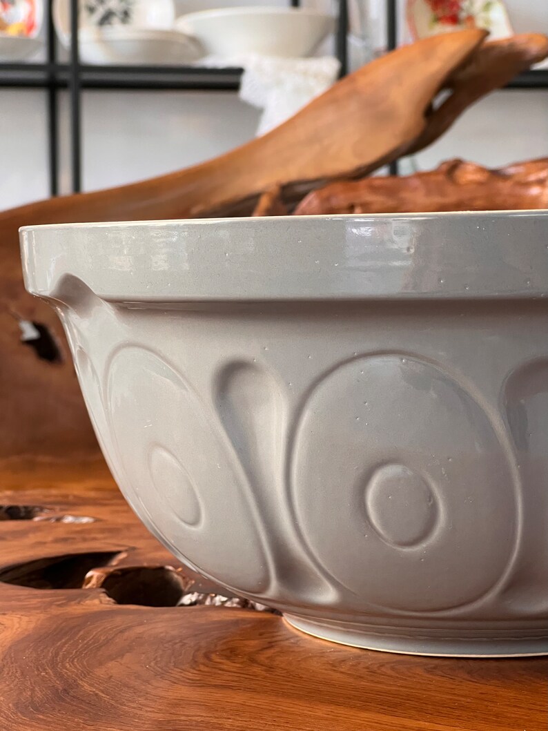 May include: A large, gray ceramic mixing bowl with a textured, rippled design. The bowl is sitting on a wooden surface.