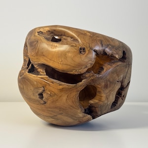 Könnte beinhalten: Eine handgeschnitzte Holzskulptur mit einer natürlichen, organischen Form. Die Skulptur hat einen ausgehöhlten Innenraum und mehrere Öffnungen, die die Maserung und Textur des Holzes zeigen. Die Farbe ist ein warmes, mittleres Braun.
