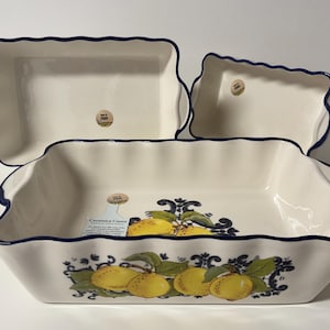Könnte beinhalten: Set aus drei weißen Keramik-Backformen mit gewelltem Rand und dunkelblauer Umrandung. Die größte Form zeigt ein Zitronen- und Blätterdesign. Die Formen sind rechteckig und unterschiedlich groß.