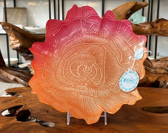 Könnte beinhalten: Eine große, korallenförmige Servierplatte mit einem rosa-orangen Ombre-Glaze. Die Platte hat ein erhabenes, strukturiertes Design, das einem Baumring ähnelt. Die Platte steht auf einem klaren Ständer und hat ein kleines Etikett mit der Aufschrift "efe"