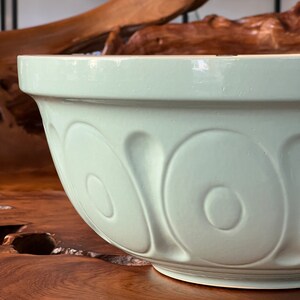 May include: A light green ceramic mixing bowl with a smooth, glossy finish. The bowl has a rounded shape and features a decorative pattern of raised circles around the sides.