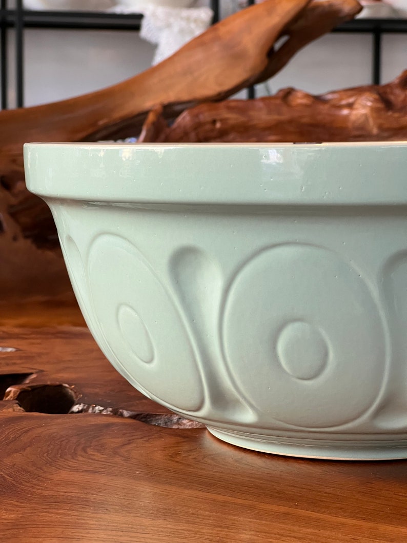 May include: A light green ceramic mixing bowl with a smooth, glossy finish. The bowl has a rounded shape and features a decorative pattern of raised circles around the sides.