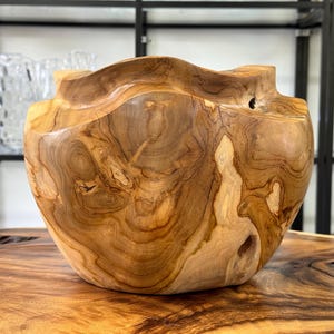 Puede incluir: Un cuenco de madera hecho a mano con una forma natural y orgánica. El cuenco está hecho de madera de color marrón claro con vetas visibles y un borde ondulado. Se apoya sobre una superficie de madera, mostrando su diseño y textura únicos. El diámetro del cuenco es de unos 30 cm.
