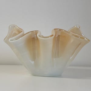 Puede incluir: Una taza de cerámica blanca con asa negra y el texto "But First, Coffee" en negrita negra. La taza se encuentra sobre un fondo borroso, sugiriendo un ambiente acogedor.
